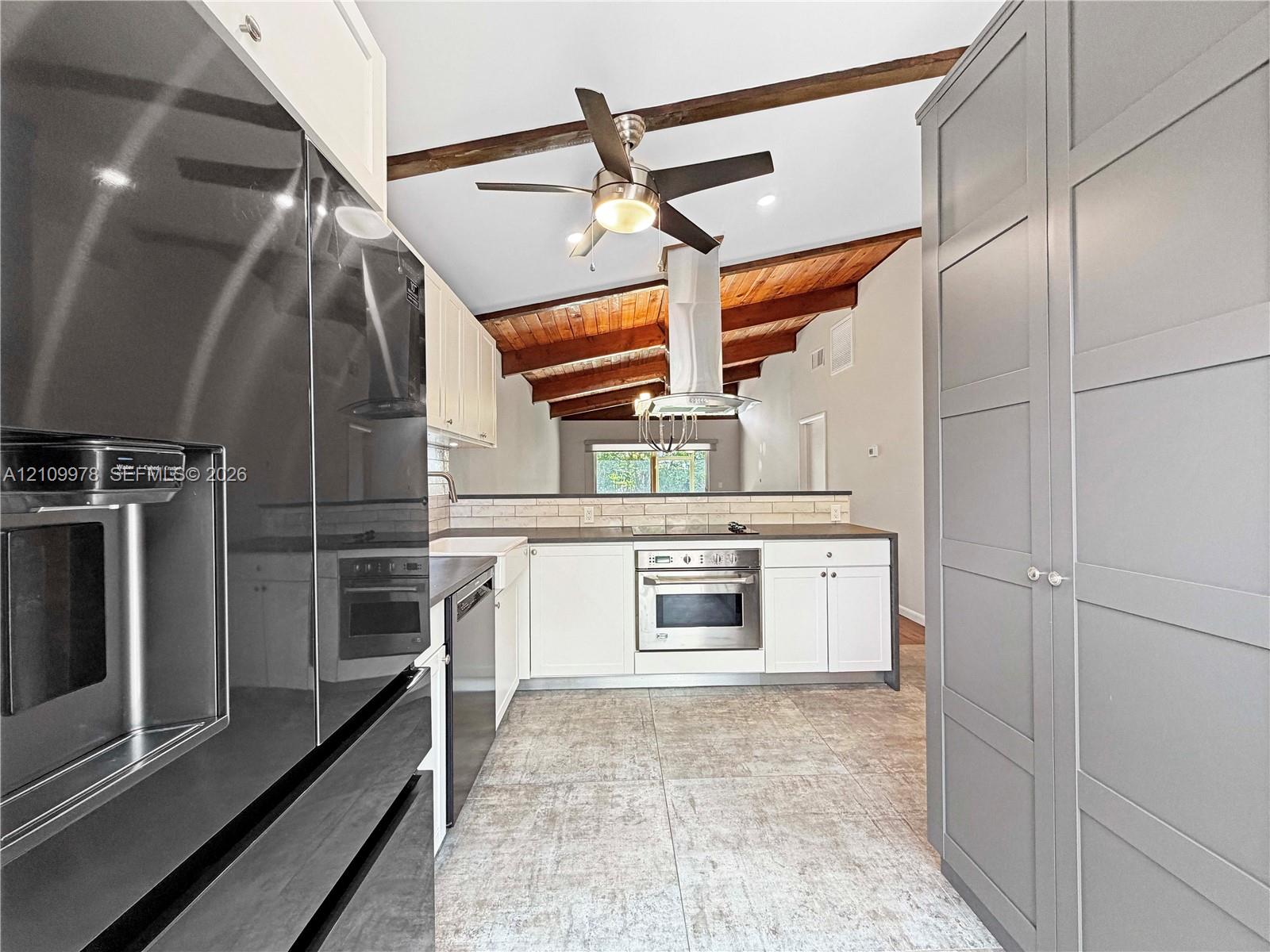 Kitchen featuring high-contrast cabinetry, stainless steel appliances, a ceiling-mounted range hood, exposed wood ceiling beams, and tile flooring Kitchen featuring high-contrast cabinetry, stainless steel appliances, a ceiling-mounted range hood, exposed wood ceiling beams, and tile flooring