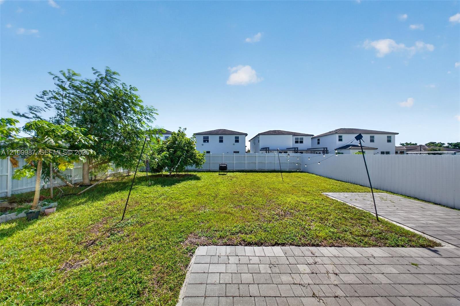 Fenced backyard featuring a manicured lawn, paver patio, and mature trees