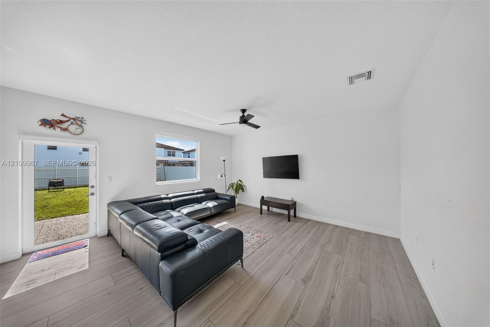 Living area featuring neutral-toned wood-finish flooring, a ceiling fan, and a glass-paneled exterior door