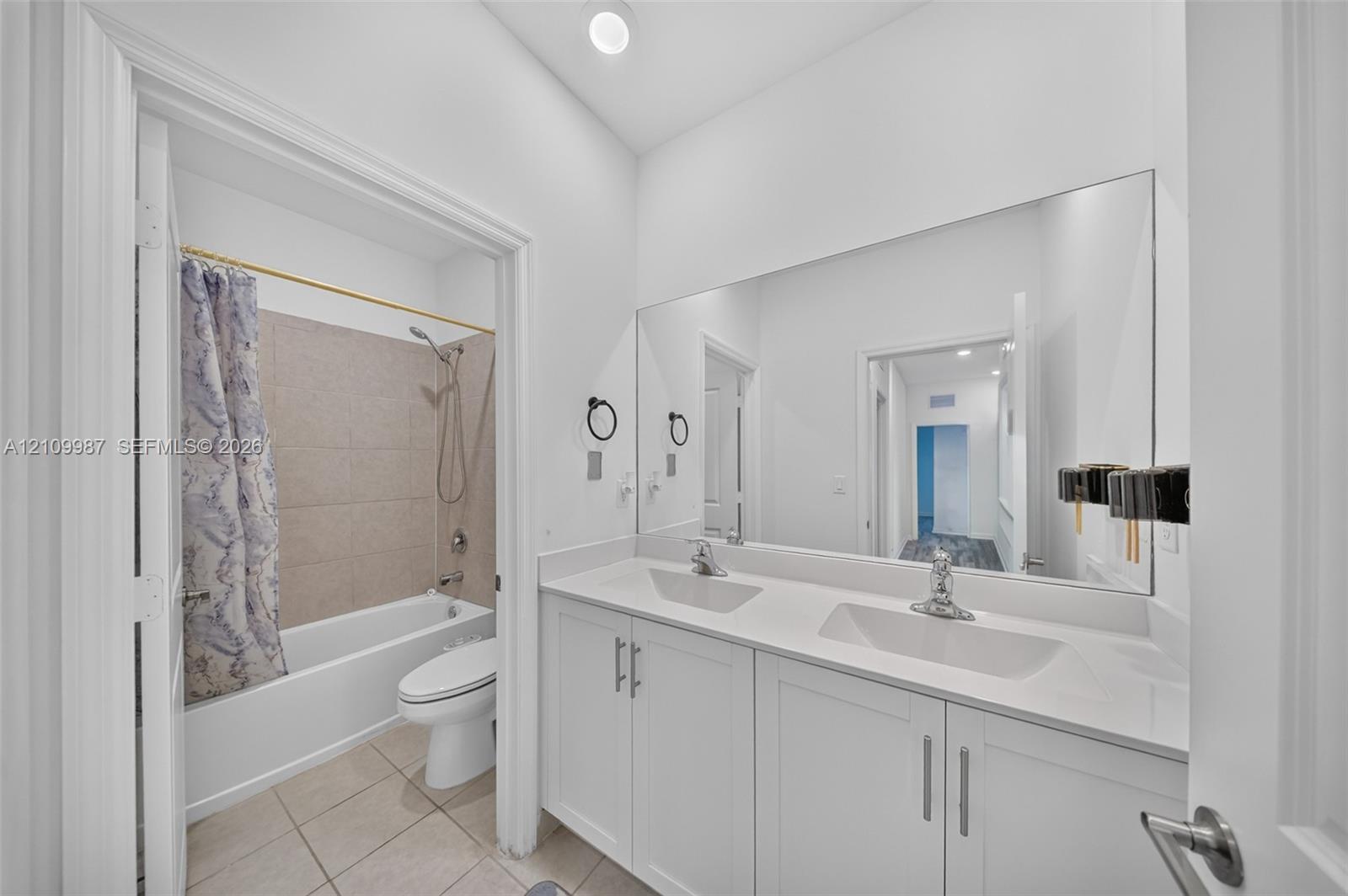 Dual-sink vanity with a solid-surface countertop, full-width wall mirror, and tub-shower combination featuring tile surround