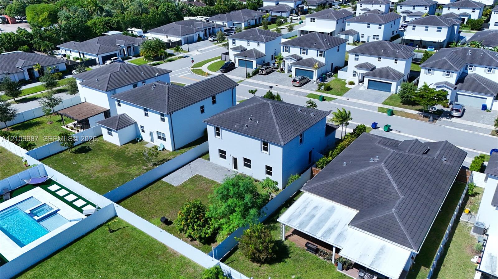 Aerial perspective of a multi-story residential property featuring a tiled roof, a private fenced yard, and a paved patio area.