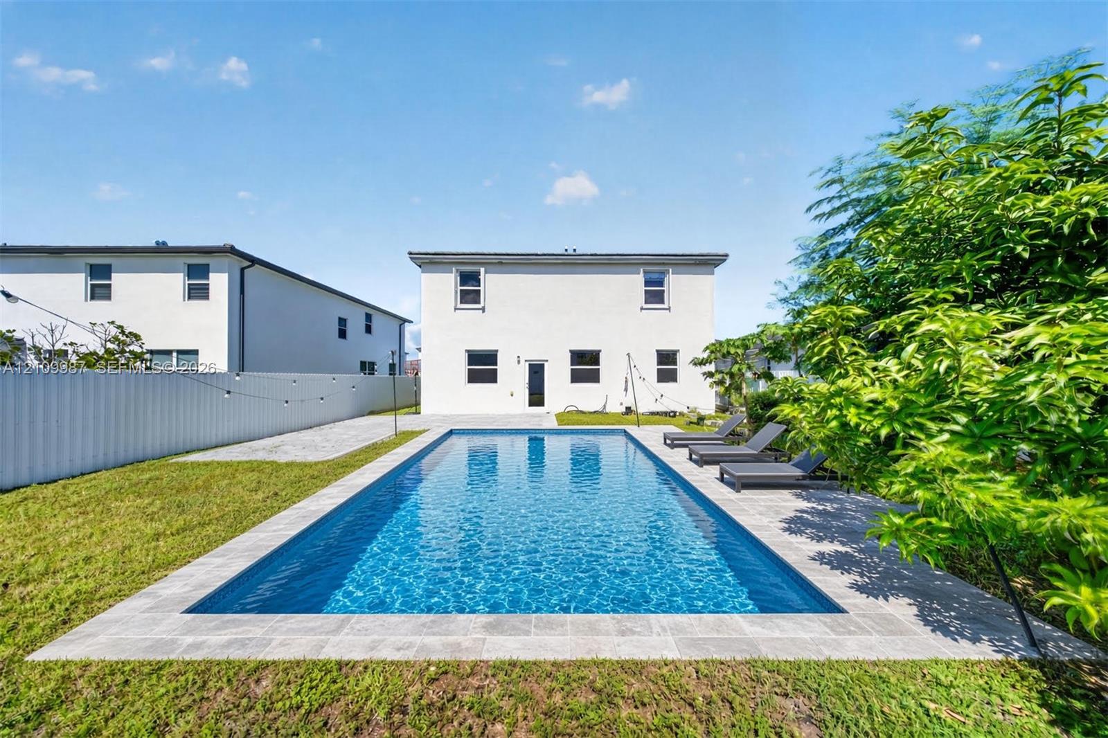 Staged Rectangular in-ground swimming pool featuring a stone-paver surround, manicured lawn, and perimeter fencing