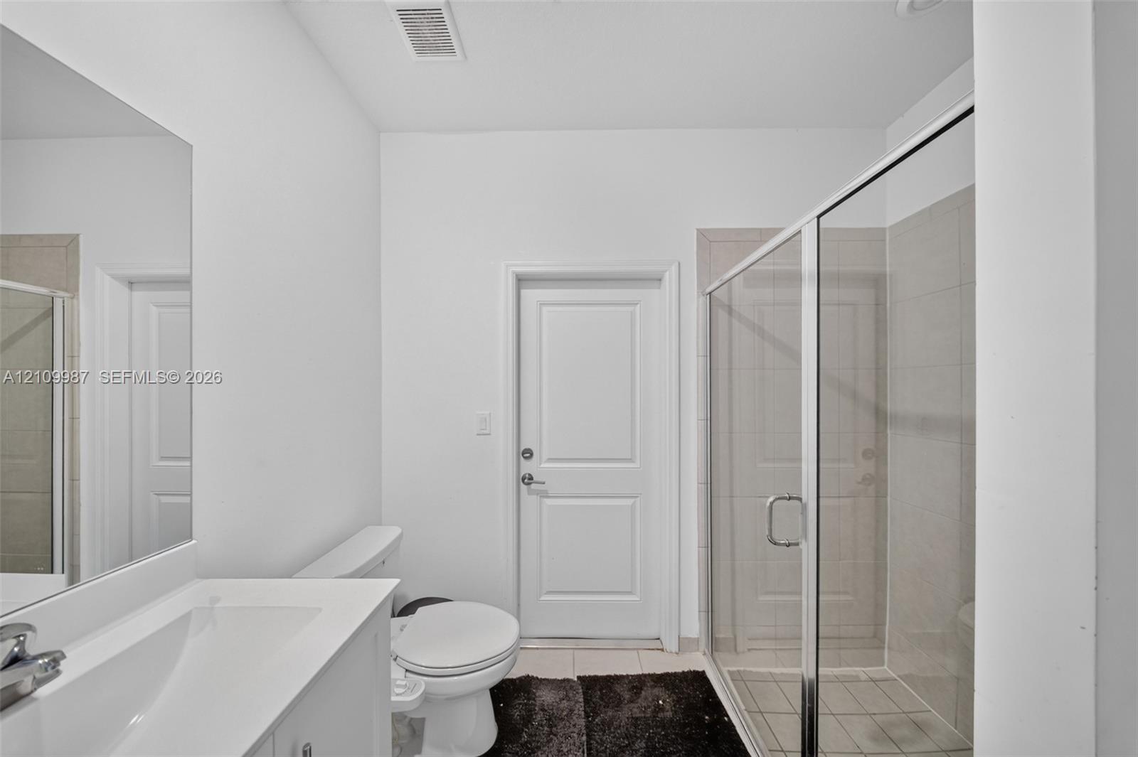 Bathroom featuring a vanity with a white countertop and integrated sink, a glass-enclosed shower with tile surround, and a wall-mounted mirror