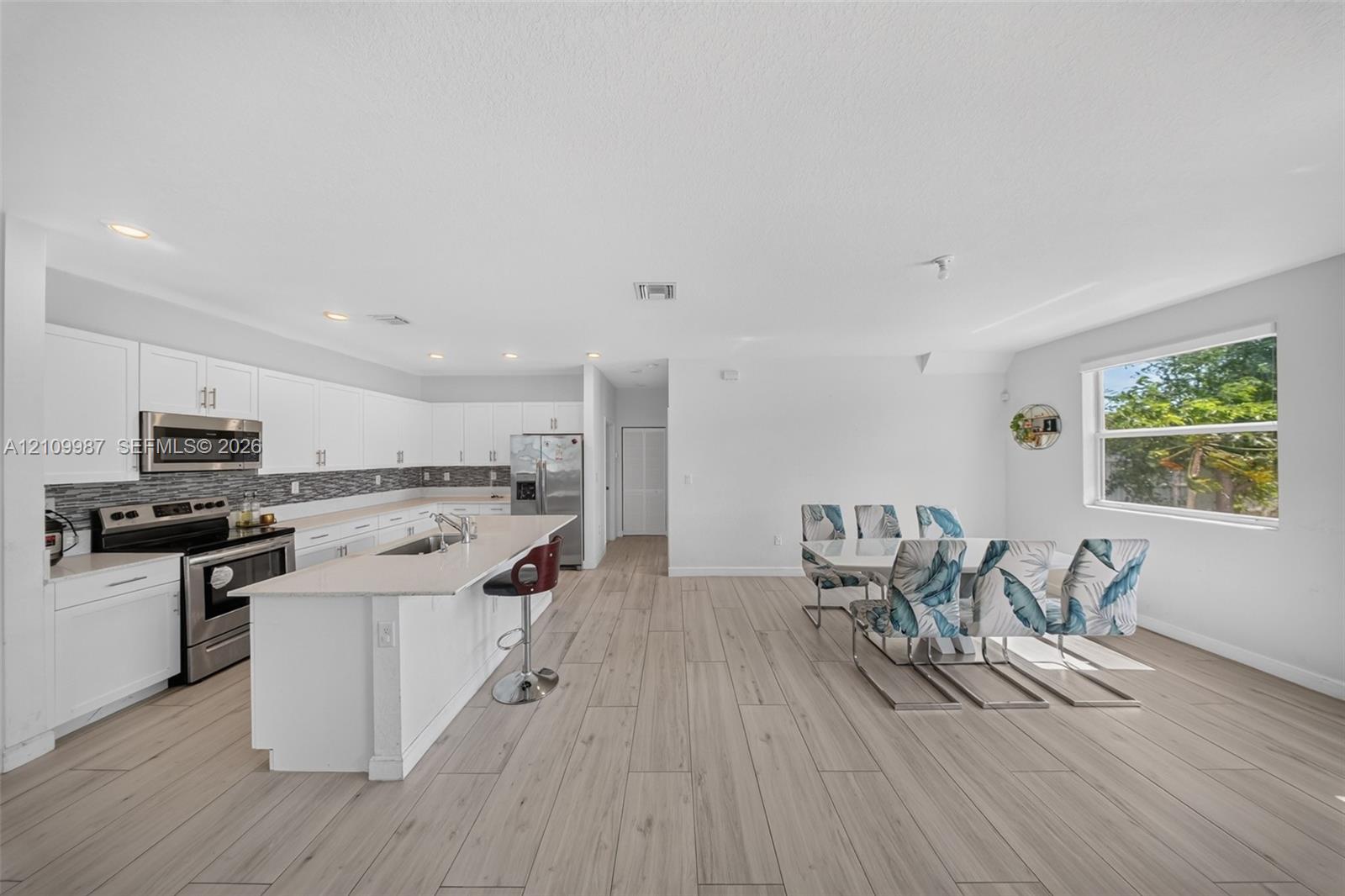 Open-concept kitchen featuring white shaker-style cabinetry, stainless steel appliances, a central island with a quartz countertop