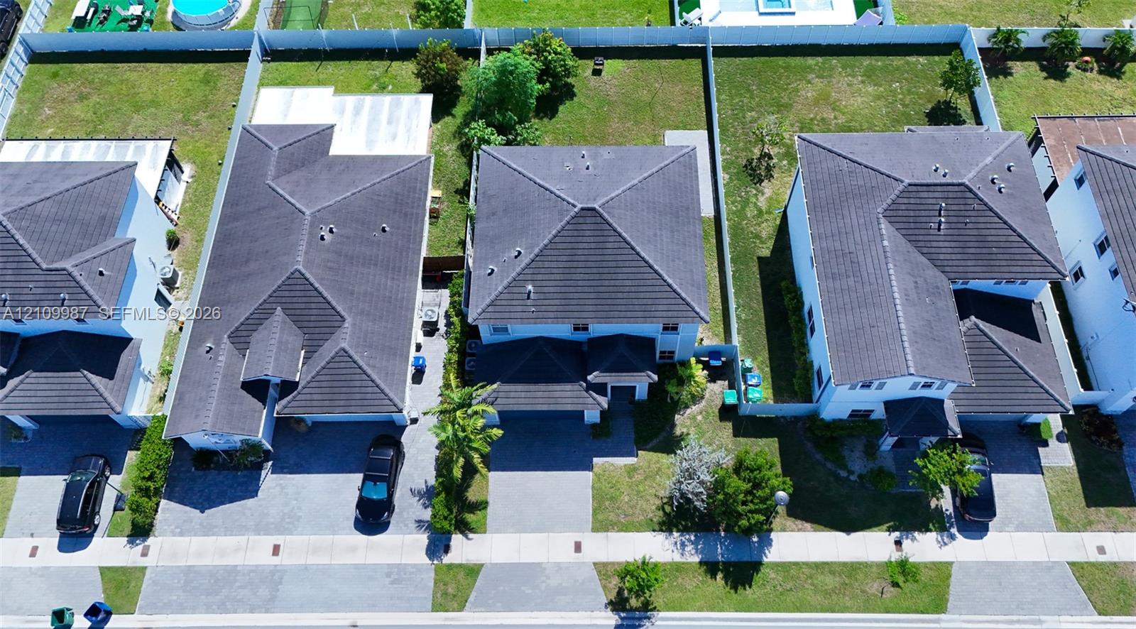 Aerial perspective of suburban properties featuring multi-level dwellings, tile roofing, paved driveways, and fenced rear grounds