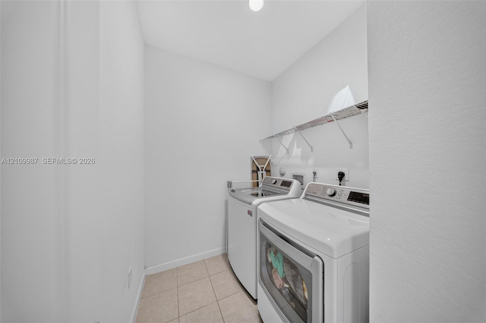 Dedicated laundry area featuring ceramic tile flooring, wall-mounted wire shelving, and appliance hookups