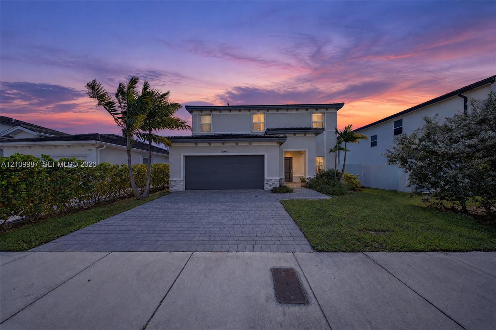 Two-story stucco exterior with stone veneer accents, multi-car garage, and a paved stone driveway