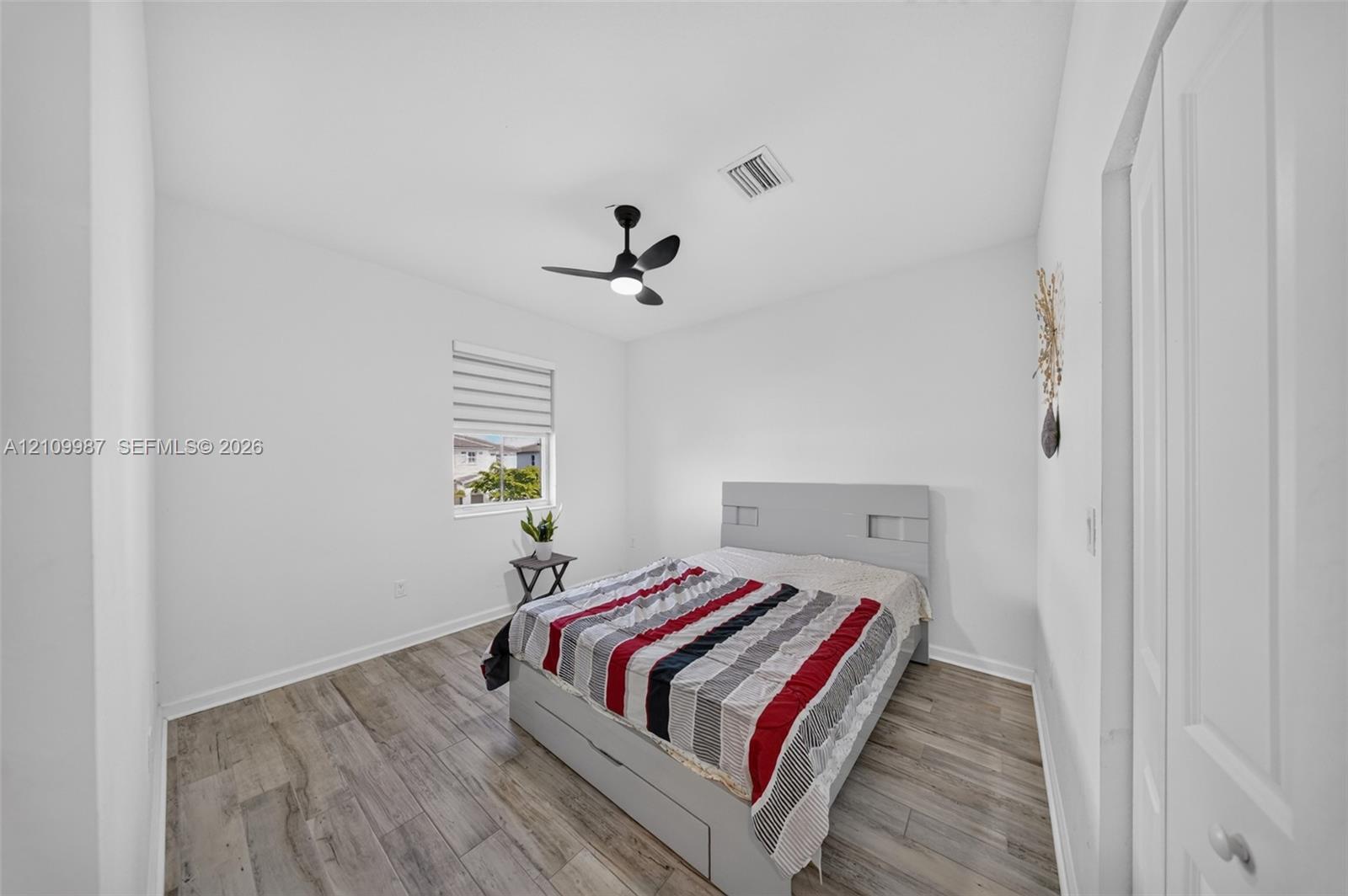 Bedroom featuring porcelain flooring, a matte black ceiling fan with integrated lighting, and a window with adjustable roller shades