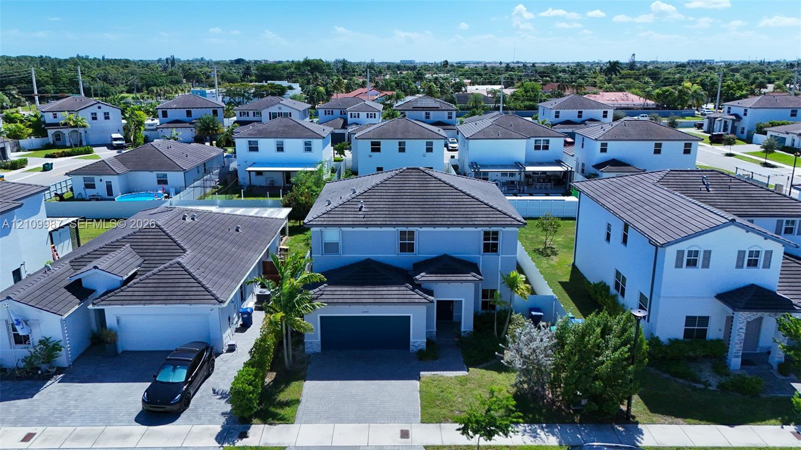 Aerial perspective of a two-story residence featuring a dark tile roof, smooth-stucco exterior, paver driveway, and a two-car garage