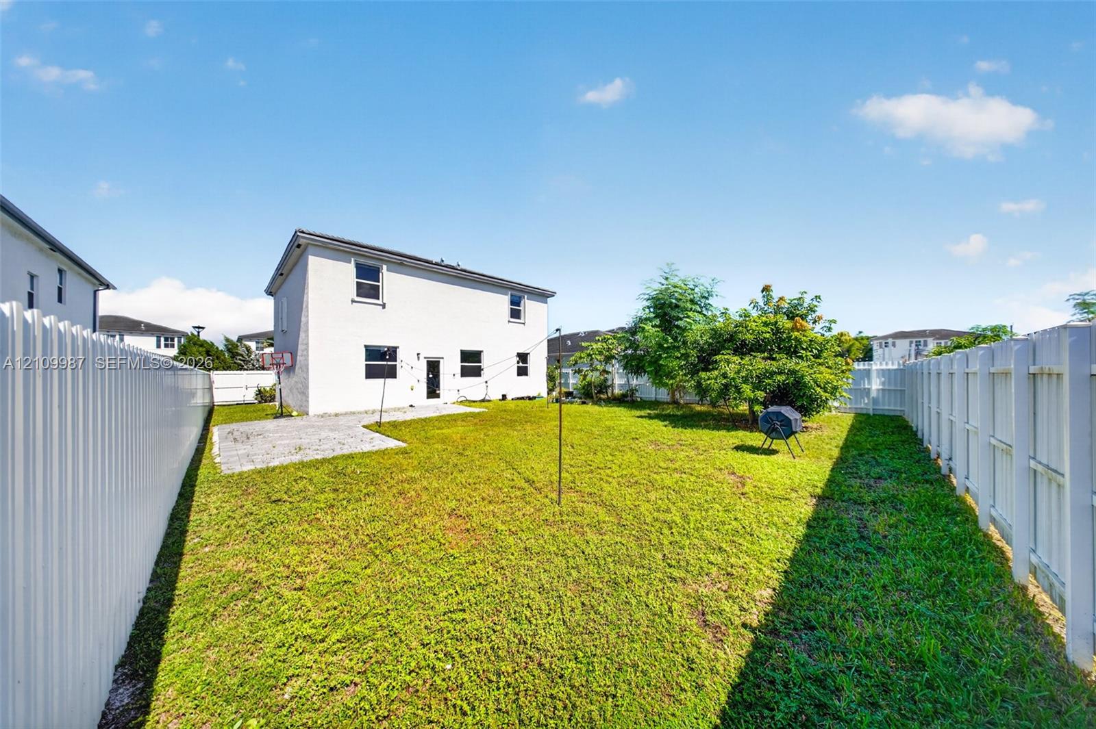 Backyard featuring a grass lawn, white vinyl fencing, and a concrete patio area