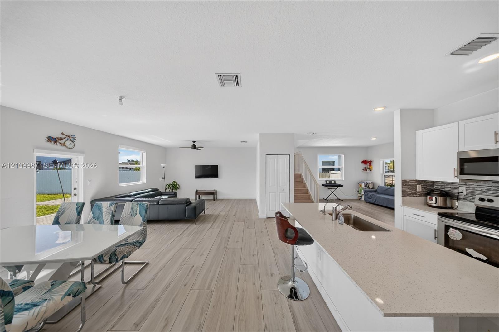 Open-concept kitchen featuring an island with a quartz countertop, white cabinetry, integrated stainless steel appliances, and porcelain tile flooring throughout