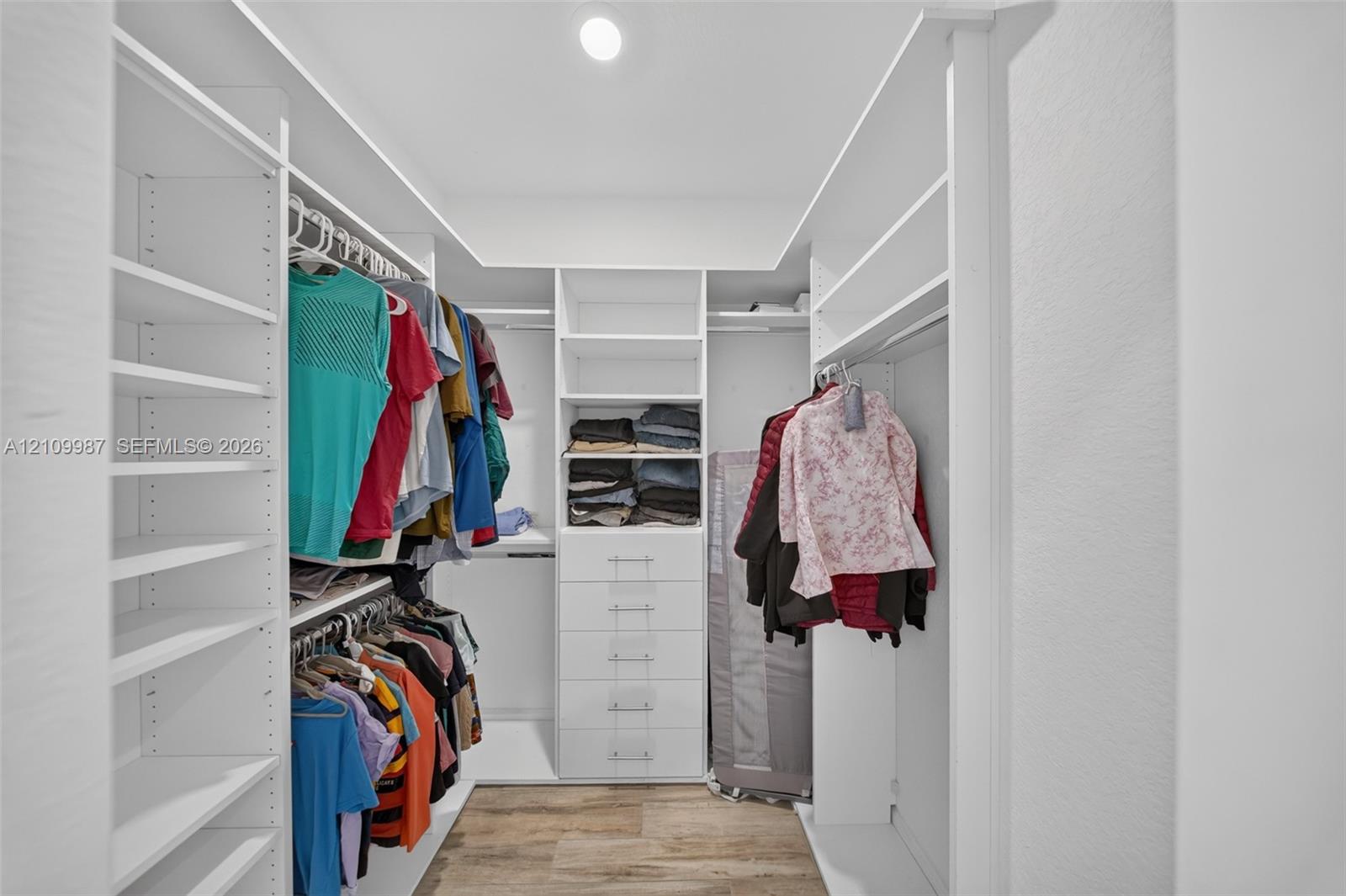 Walk-in closet featuring white custom built-in shelving, a dedicated drawer stack, overhead lighting, and porcelain flooring