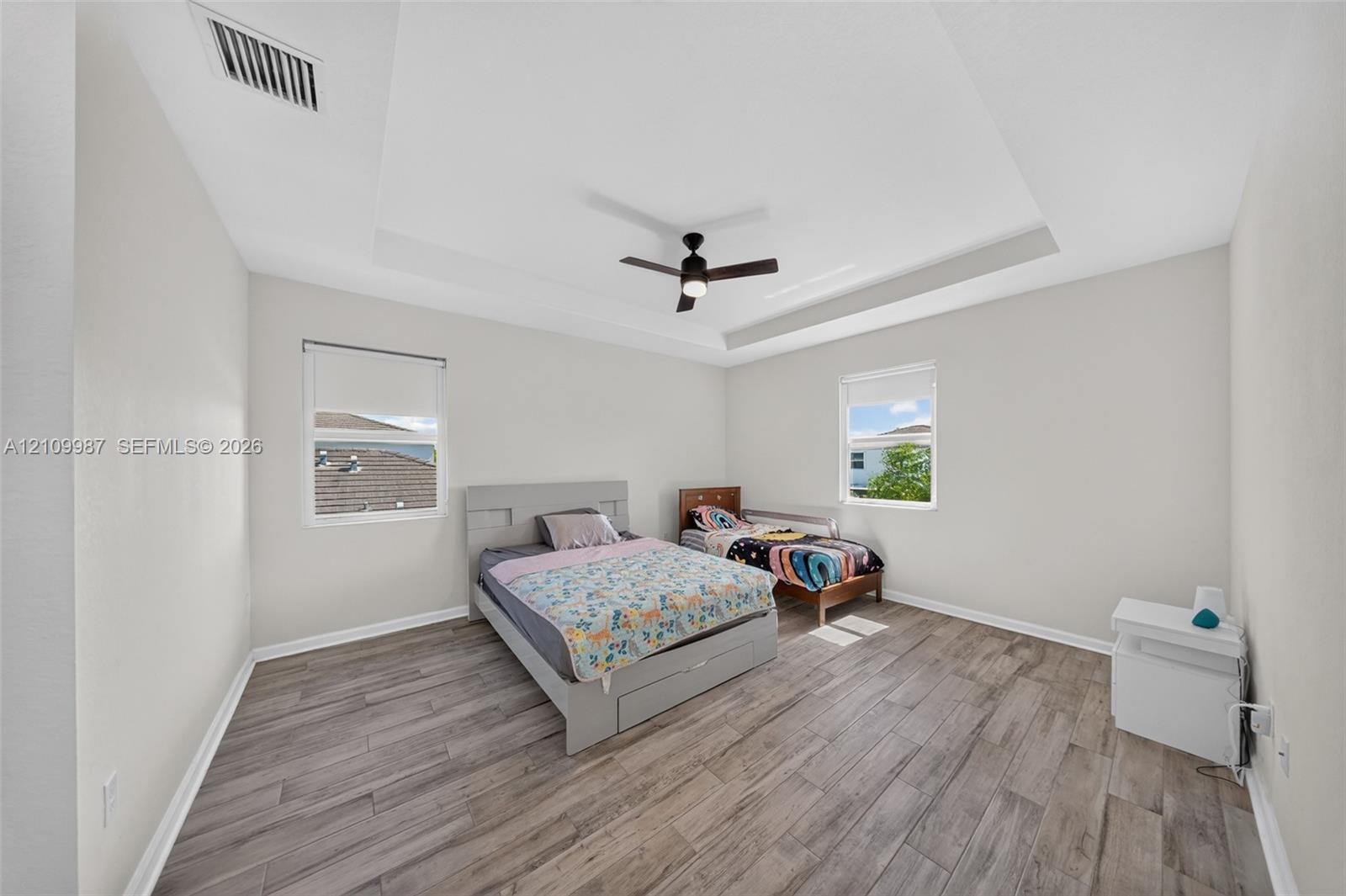 Room interior featuring tray ceiling, porcelain tile flooring, and integrated ceiling fan with light fixture