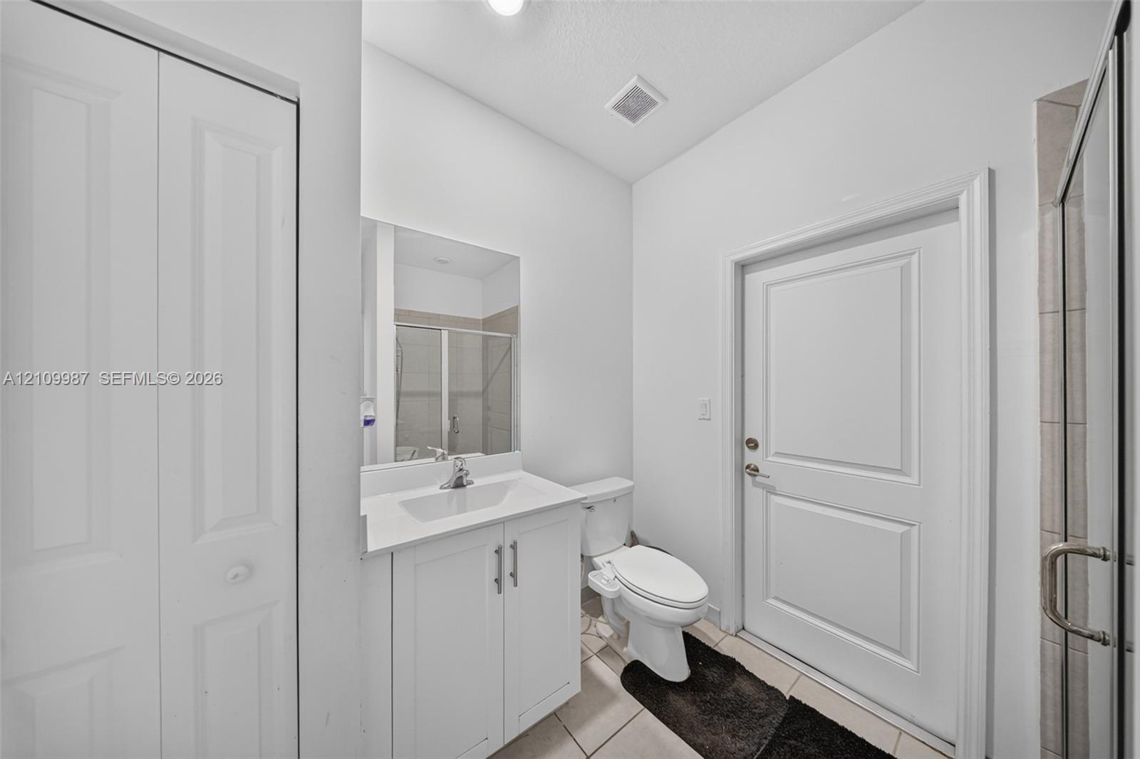 Bathroom featuring a white vanity cabinet with an integrated sink, polished chrome faucet, rectangular wall mirror, tile flooring, and a glass-enclosed shower
