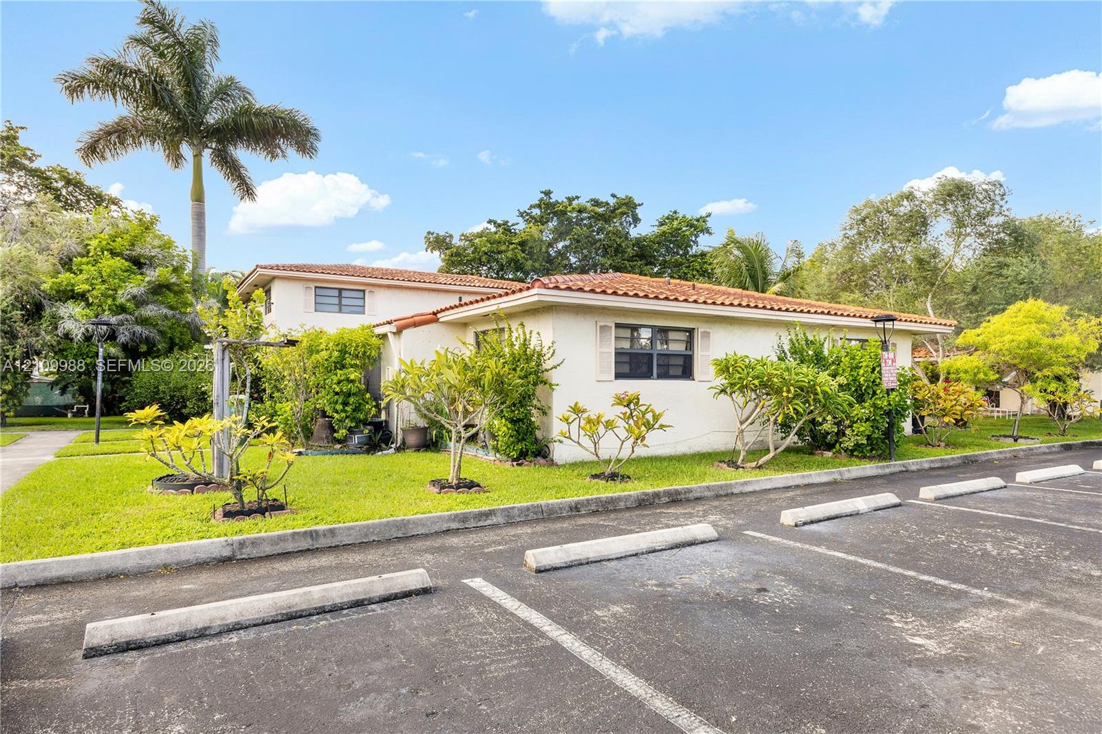Stucco exterior featuring a terracotta tile roof, designated asphalt parking spaces, and established landscaping with mature palm trees Stucco exterior featuring a terracotta tile roof, designated asphalt parking spaces, and established landscaping with mature palm trees