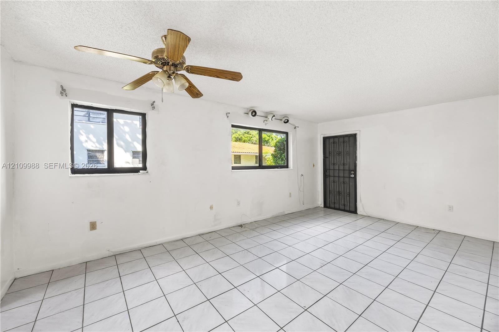 Interior space featuring white tile flooring, ceiling fan with light fixture, multi-pane windows, and a metal security door Interior space featuring white tile flooring, ceiling fan with light fixture, multi-pane windows, and a metal security door