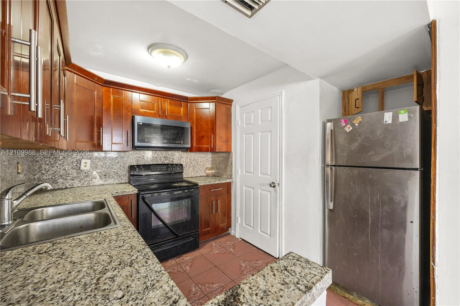 Kitchen featuring wood cabinetry, stone-surface countertops, dual-basin stainless steel sink, tile flooring, and stainless steel appliances Kitchen featuring wood cabinetry, stone-surface countertops, dual-basin stainless steel sink, tile flooring, and stainless steel appliances