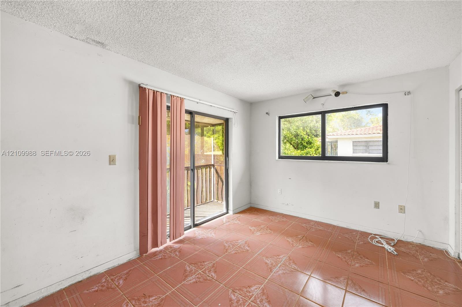 Interior room featuring large-format terra cotta tile flooring, sliding glass door with external screen, and horizontal windows with black frames Interior room featuring large-format terra cotta tile flooring, sliding glass door with external screen, and horizontal windows with black frames