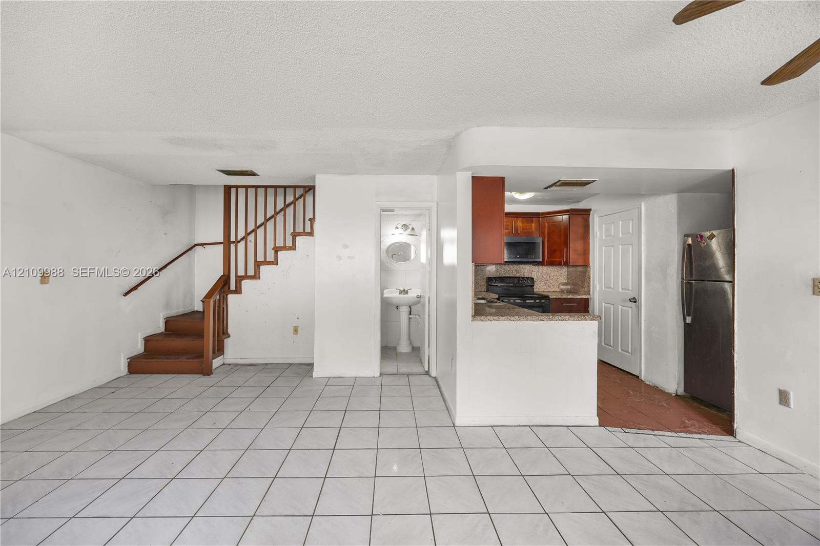 Interior featuring white tile flooring, wooden staircase with matching handrail, kitchen with dark wood cabinetry and stone countertops, and a pedestal sink Interior featuring white tile flooring, wooden staircase with matching handrail, kitchen with dark wood cabinetry and stone countertops, and a pedestal sink