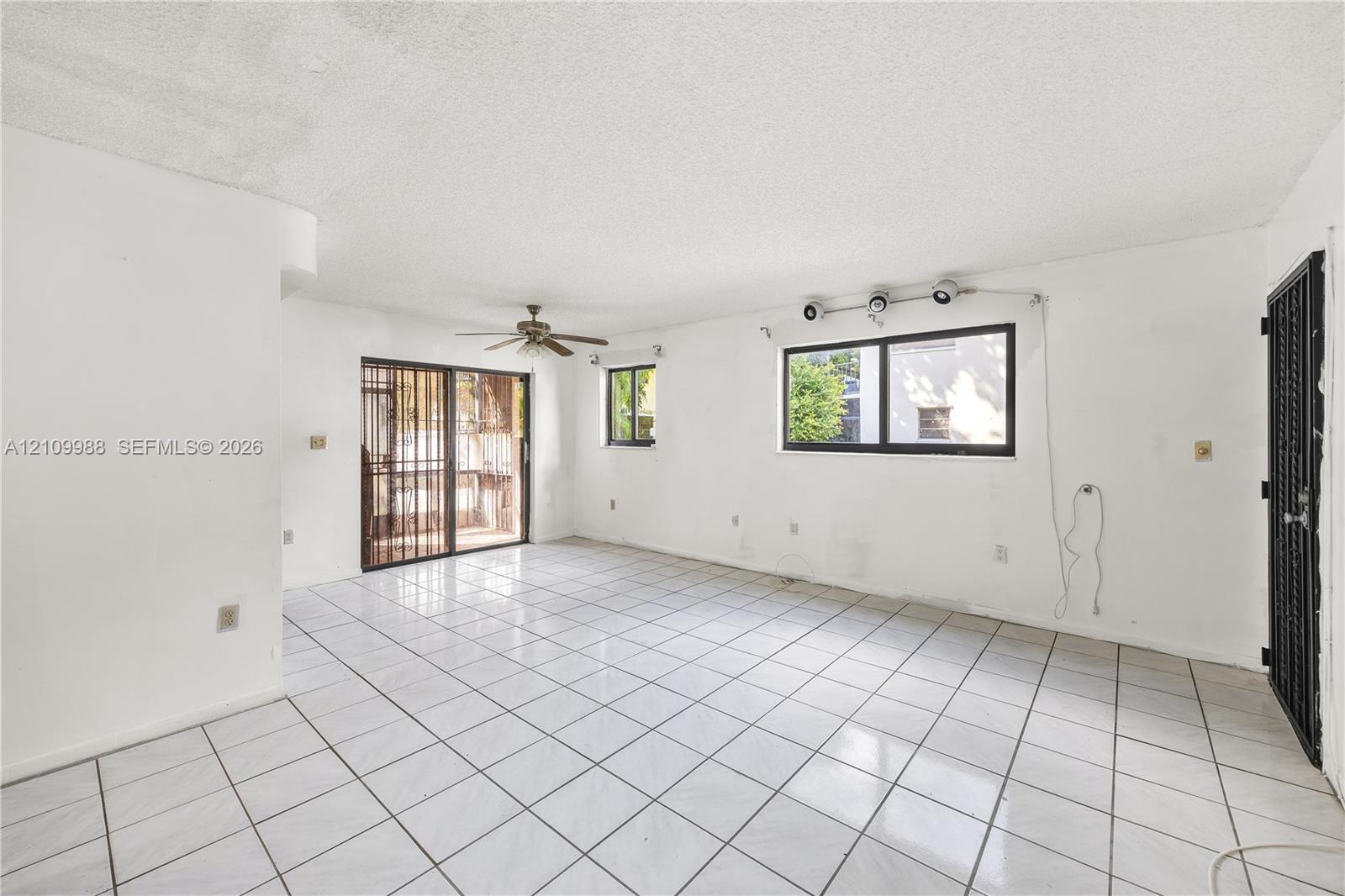 Interior space featuring large-format ceramic tile flooring, a multi-blade ceiling fan, metal security door, and sliding glass patio door Interior space featuring large-format ceramic tile flooring, a multi-blade ceiling fan, metal security door, and sliding glass patio door