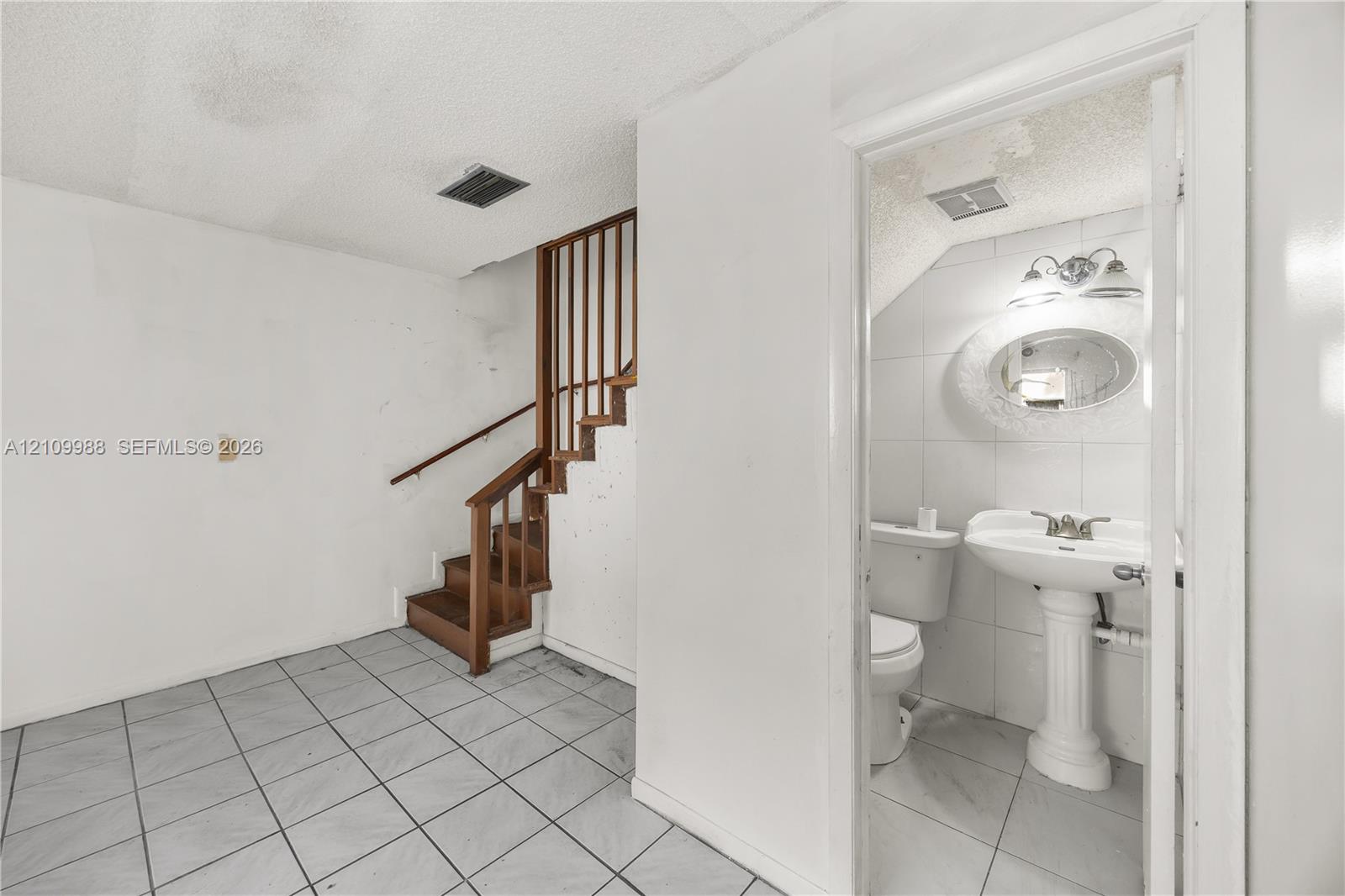 Staircase with wood railings and matching treads, tile flooring, pedestal sink, wall-mounted mirror, and wall-mounted light fixture Staircase with wood railings and matching treads, tile flooring, pedestal sink, wall-mounted mirror, and wall-mounted light fixture