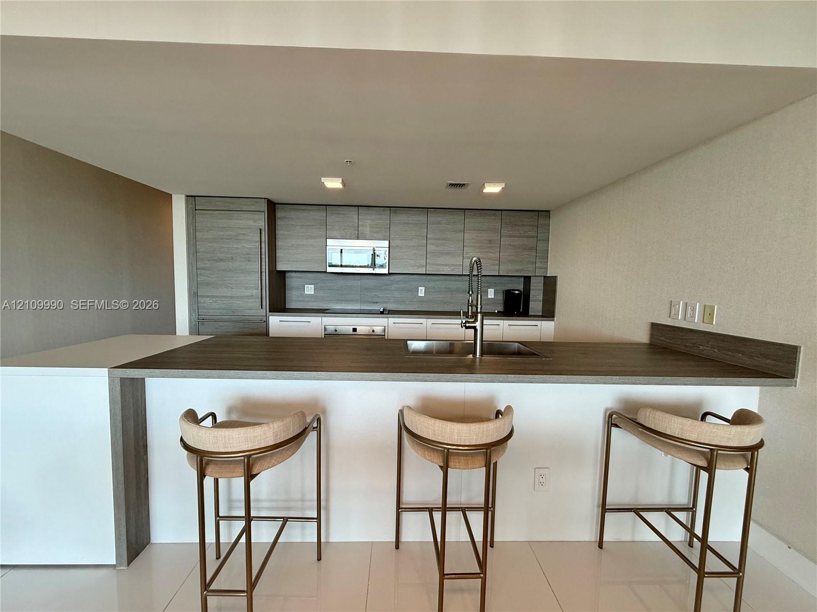 Kitchen featuring wood-finish cabinetry, integrated appliances, a waterfall-edge peninsula with a dark countertop, and polished tile flooring