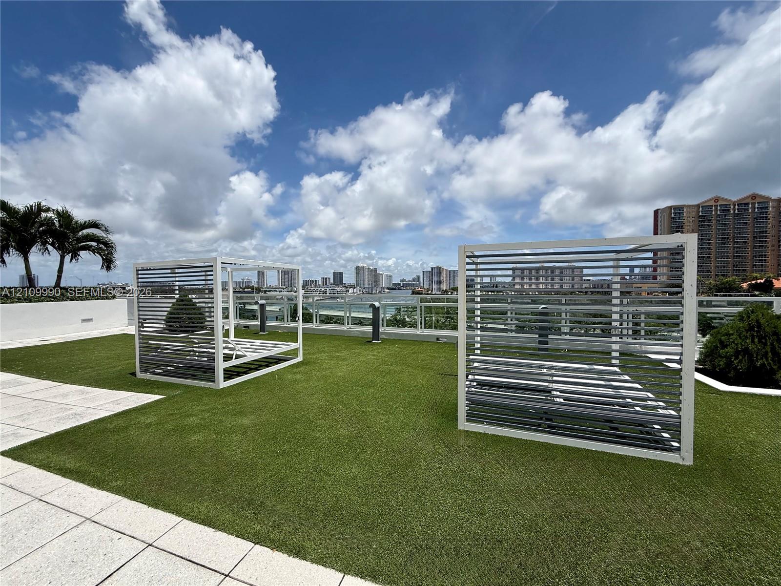 Rooftop terrace featuring synthetic turf, glass panel railings, and white metal louvered privacy structures