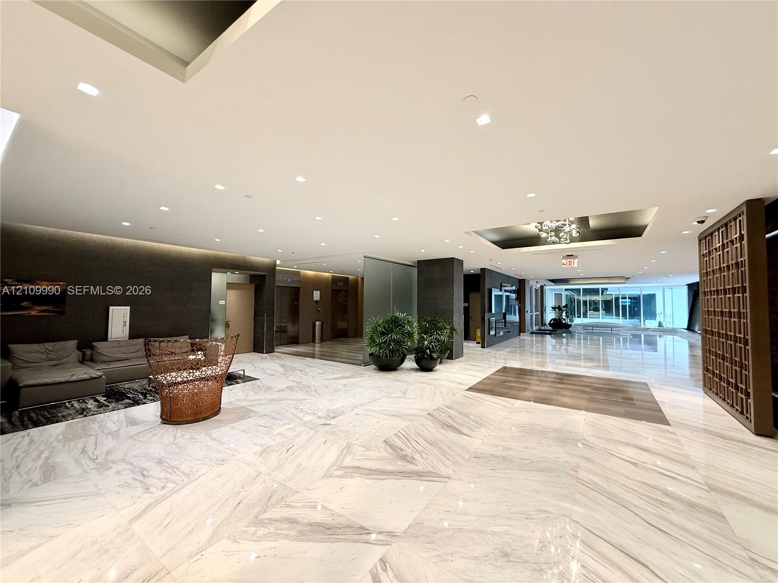 Expansive lobby featuring large-format stone tile flooring, recessed ceiling lighting, a decorative geometric wood screen, and high-gloss finishes