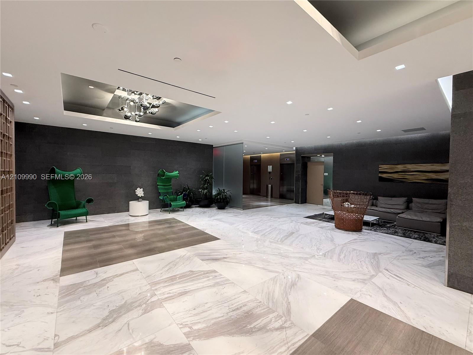 Lobby featuring large-format marble flooring, recessed ceiling lighting with sculptural chandelier, dark stone wall accents, and elevator bank