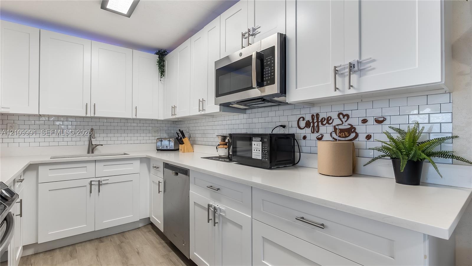 Kitchen featuring white shaker-style cabinetry, solid-surface countertops, a white subway tile backsplash, stainless steel appliances, and wood-finish flooring