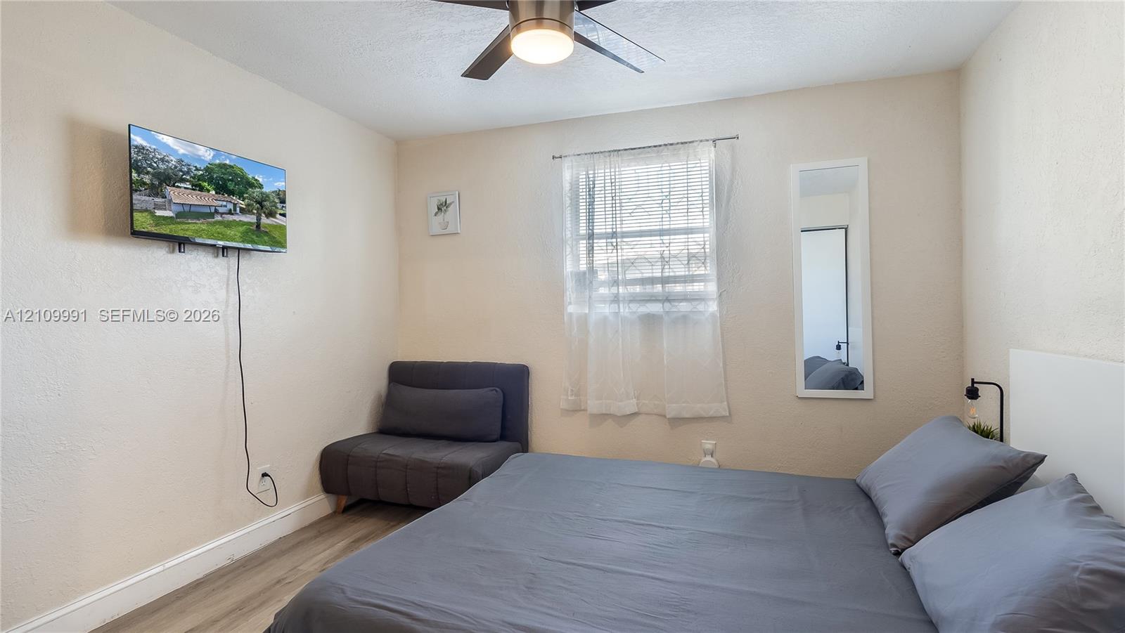 Room featuring wood-finish flooring, a ceiling fan with integrated lighting, and a single window with a horizontal blind