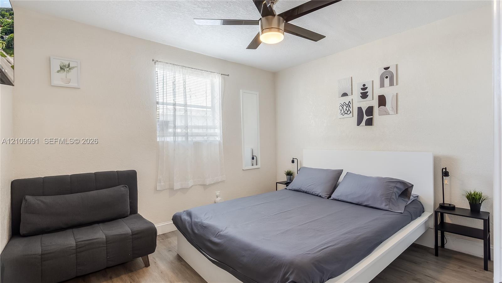 Neutral-toned room featuring wood-finish flooring, a ceiling fan with integrated lighting, and a single window