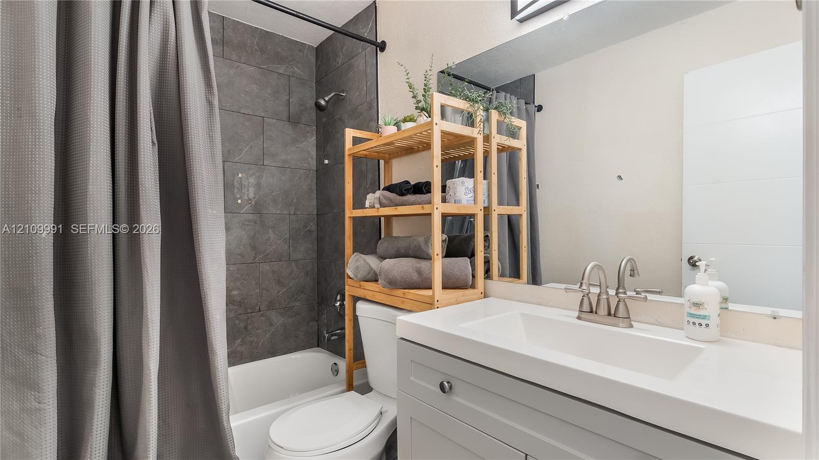 Bathroom featuring a gray vanity with a white countertop and integrated sink, a large wall-mounted mirror, and a tub-shower surround finished with large-format gray tile