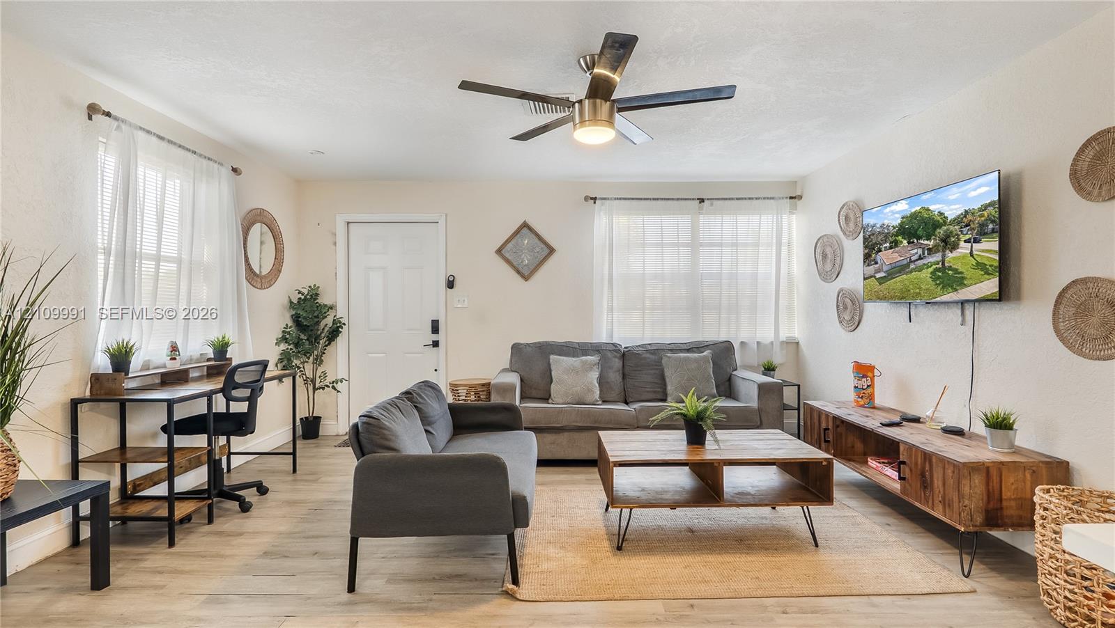 Living area featuring wood-finish flooring, a neutral color palette, dual windows with natural light, and a ceiling fan with integrated lighting