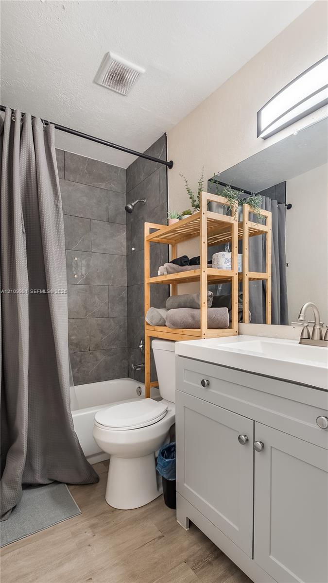 Light gray cabinetry with brushed metal hardware, white countertop, integrated sink with arched faucet, rectangular tile shower surround, and wood-finish flooring
