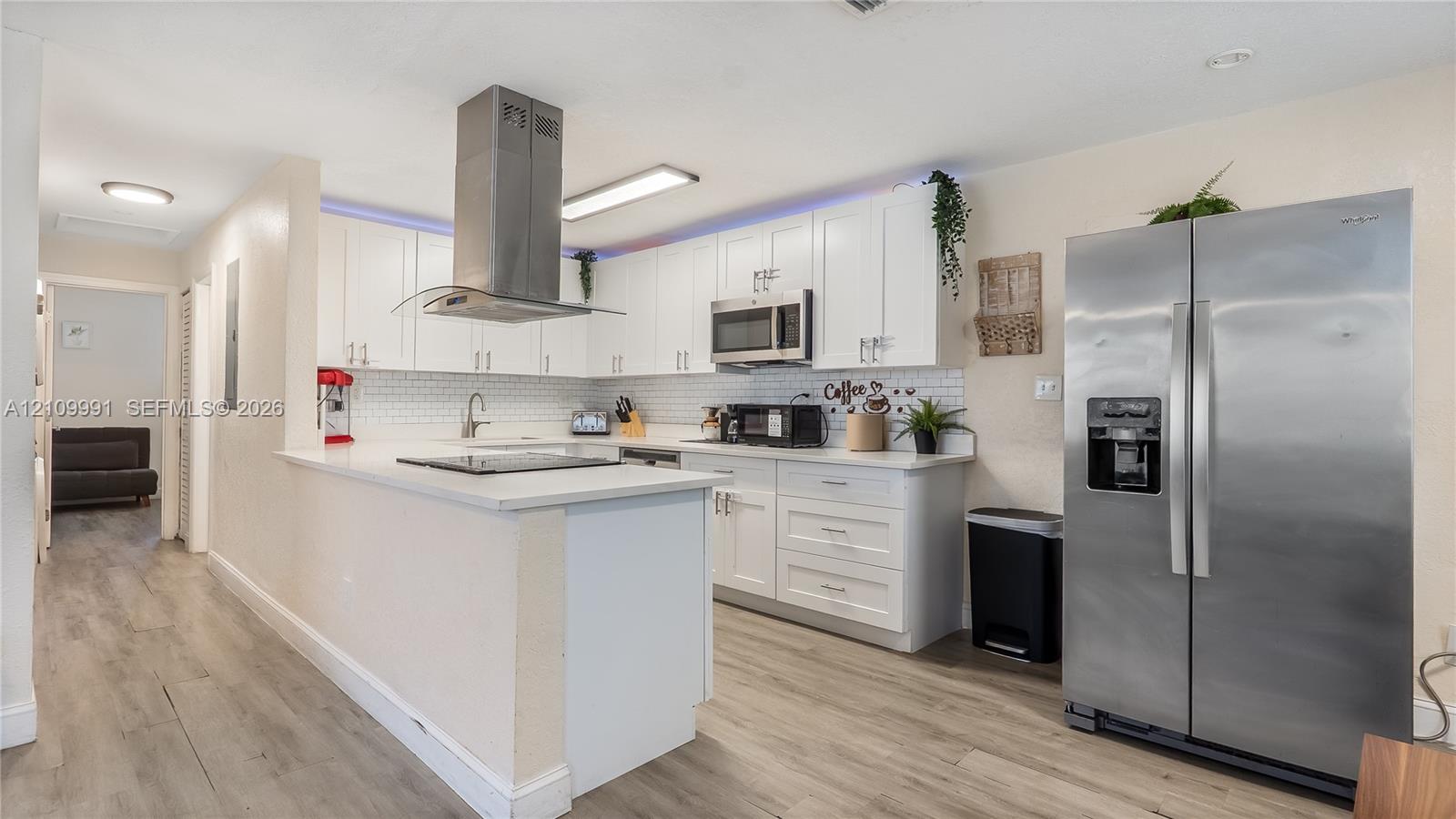 Kitchen featuring white shaker cabinetry, stainless steel appliances, a chimney-style range hood, white subway tile backsplash, and light-tone wood-finish flooring