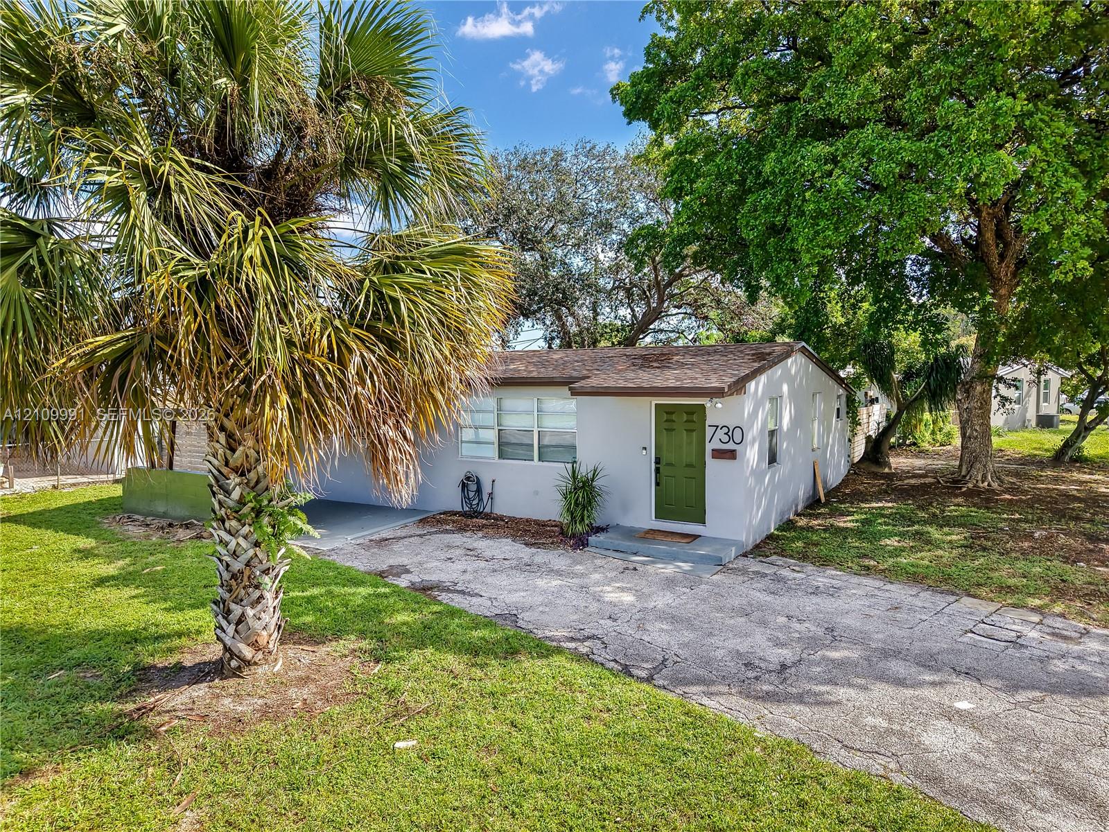 Single-story residence featuring a painted stucco exterior, a shingled roof, a paved driveway, and established trees