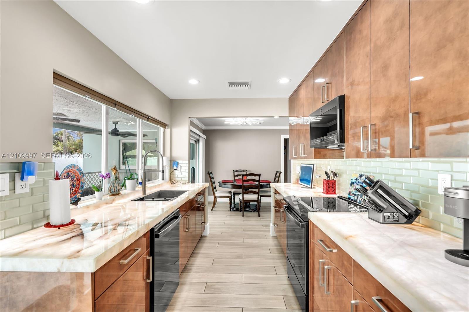 Kitchen featuring high-gloss slab cabinetry, light-toned stone-surface countertops, glass subway tile backsplash, ceramic tile flooring, and integrated black appliances