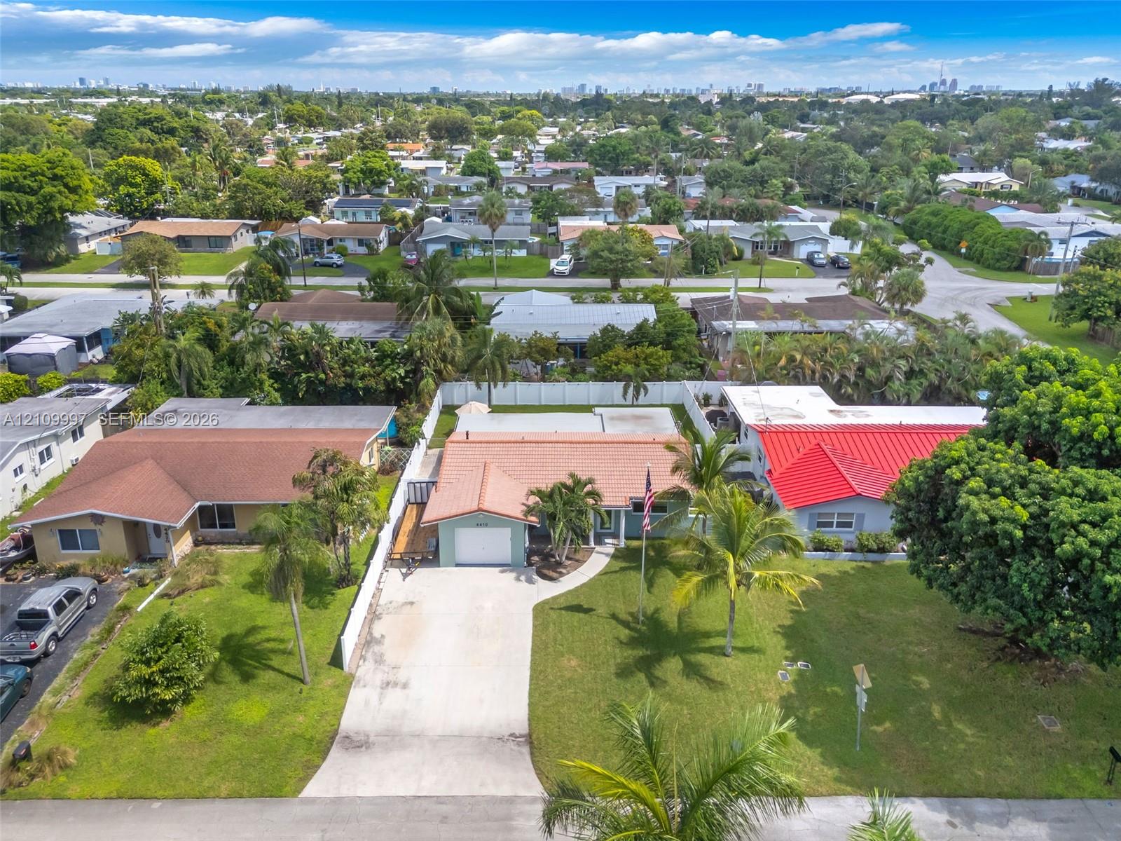 Single-story residence featuring a concrete tile roof, attached one-car garage, concrete driveway, white privacy fencing, and mature palm trees