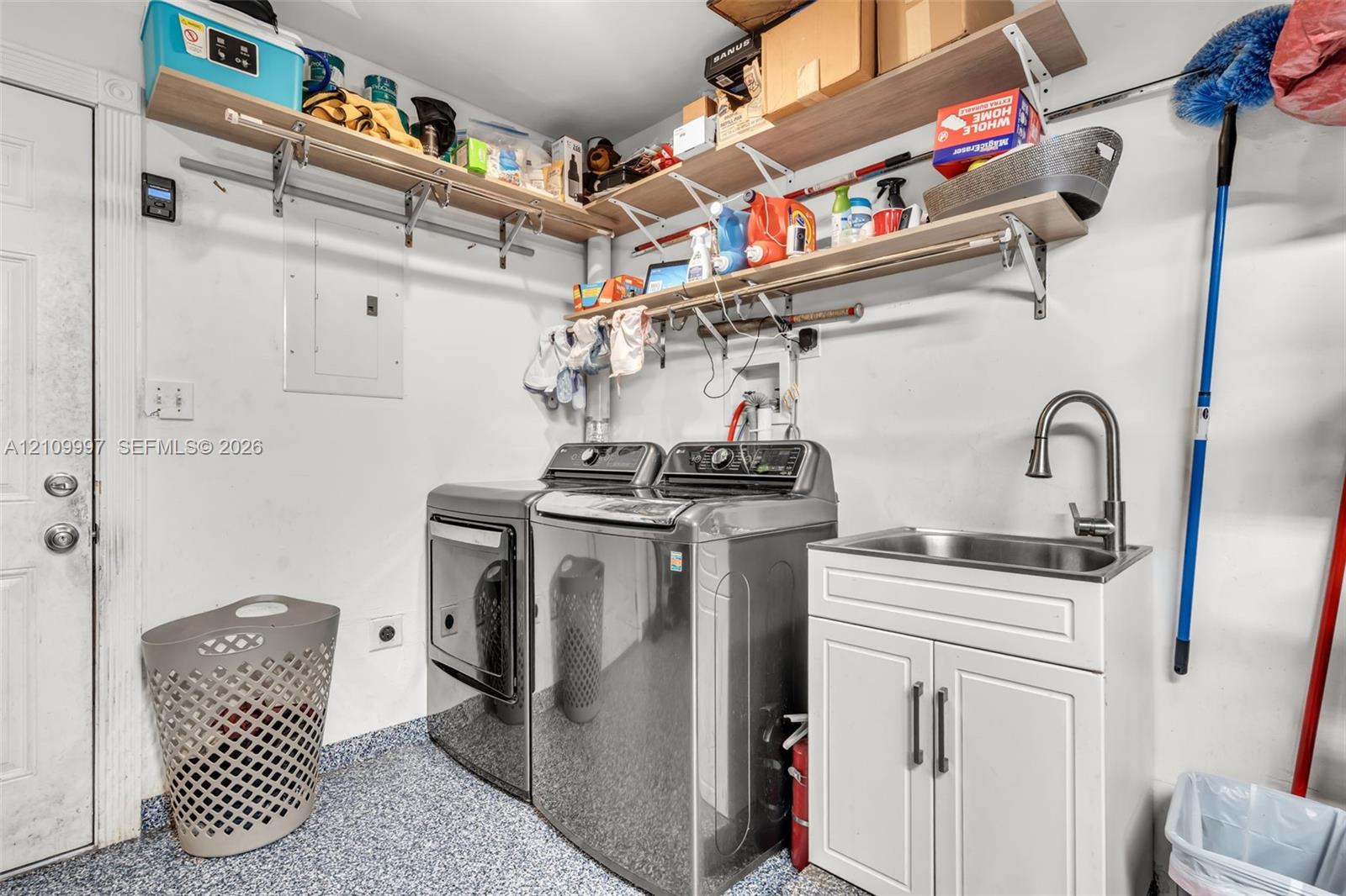 Utility space featuring epoxy flooring, built-in shelving, and a stainless steel utility sink with a high-arch faucet