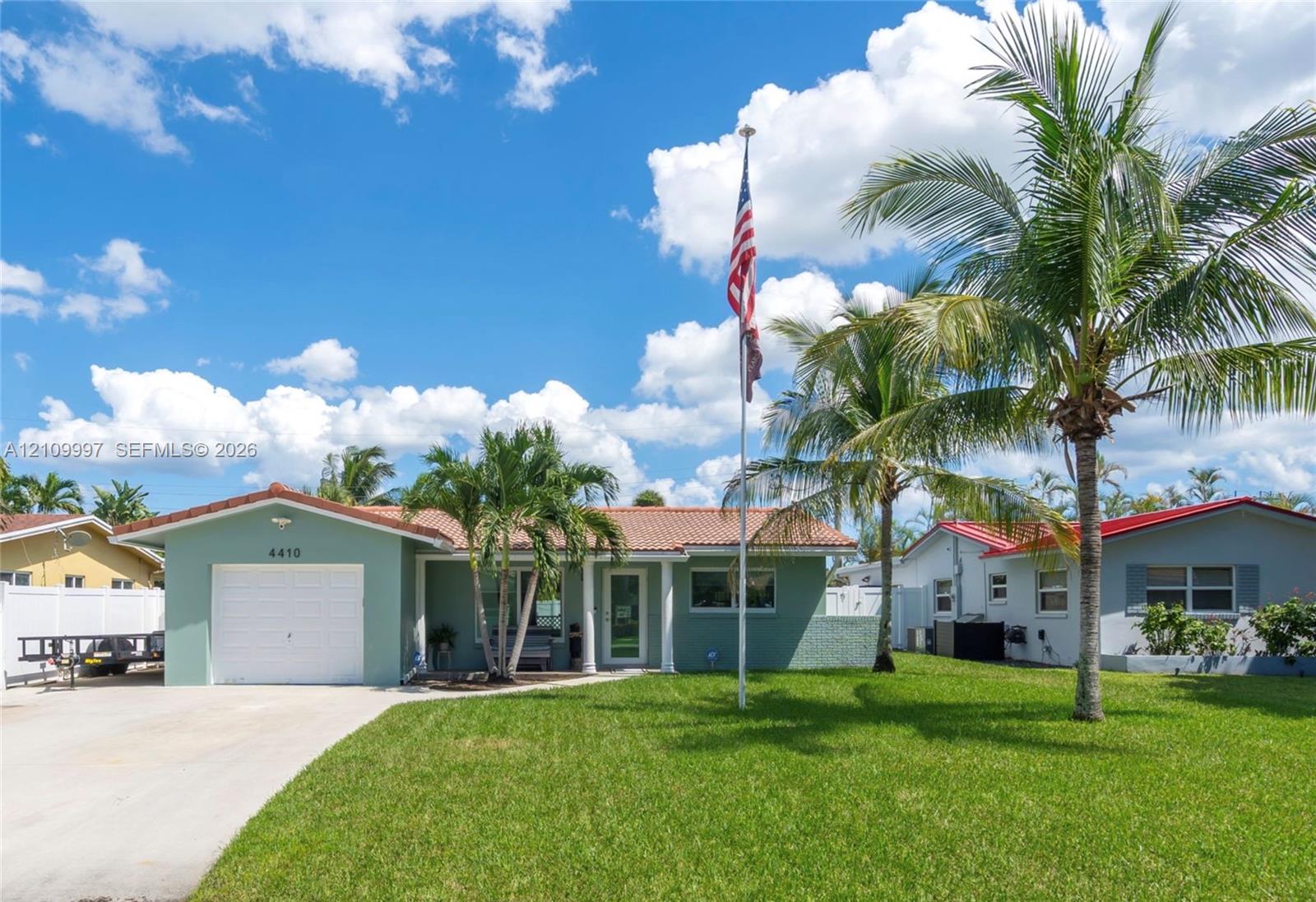 Single-story exterior featuring a clay tile roof, stucco facade, concrete driveway, and established palm trees