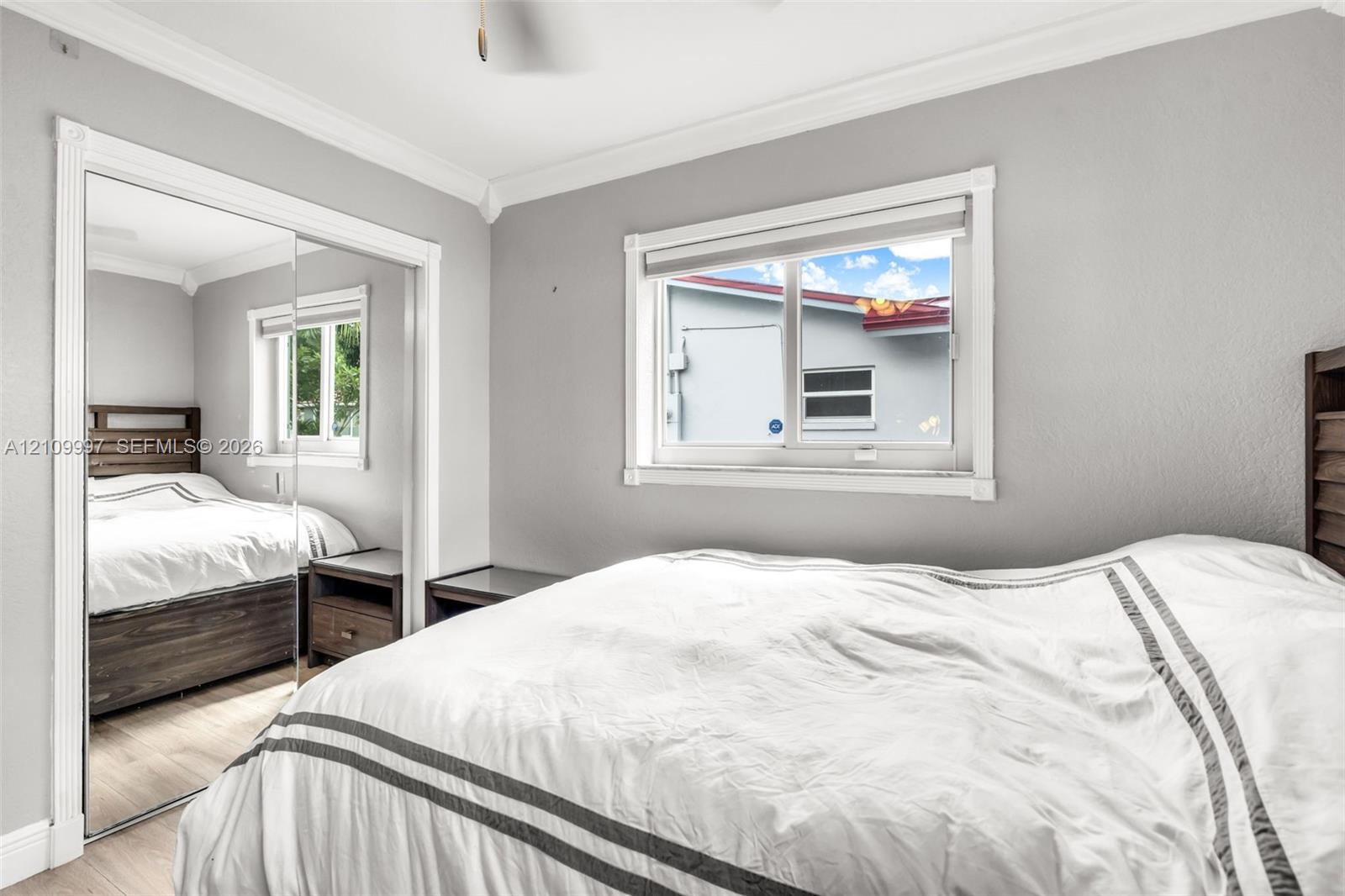 Room featuring neutral paint, crown molding, wood-finish flooring, and a sliding mirrored closet door