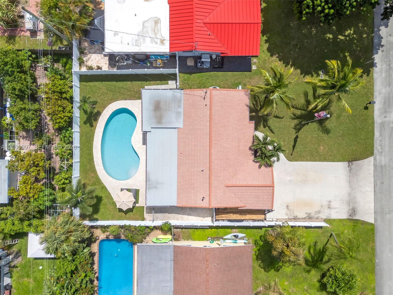 Aerial view featuring a residential property with a kidney-shaped in-ground pool, expansive backyard, concrete driveway, and tile roof