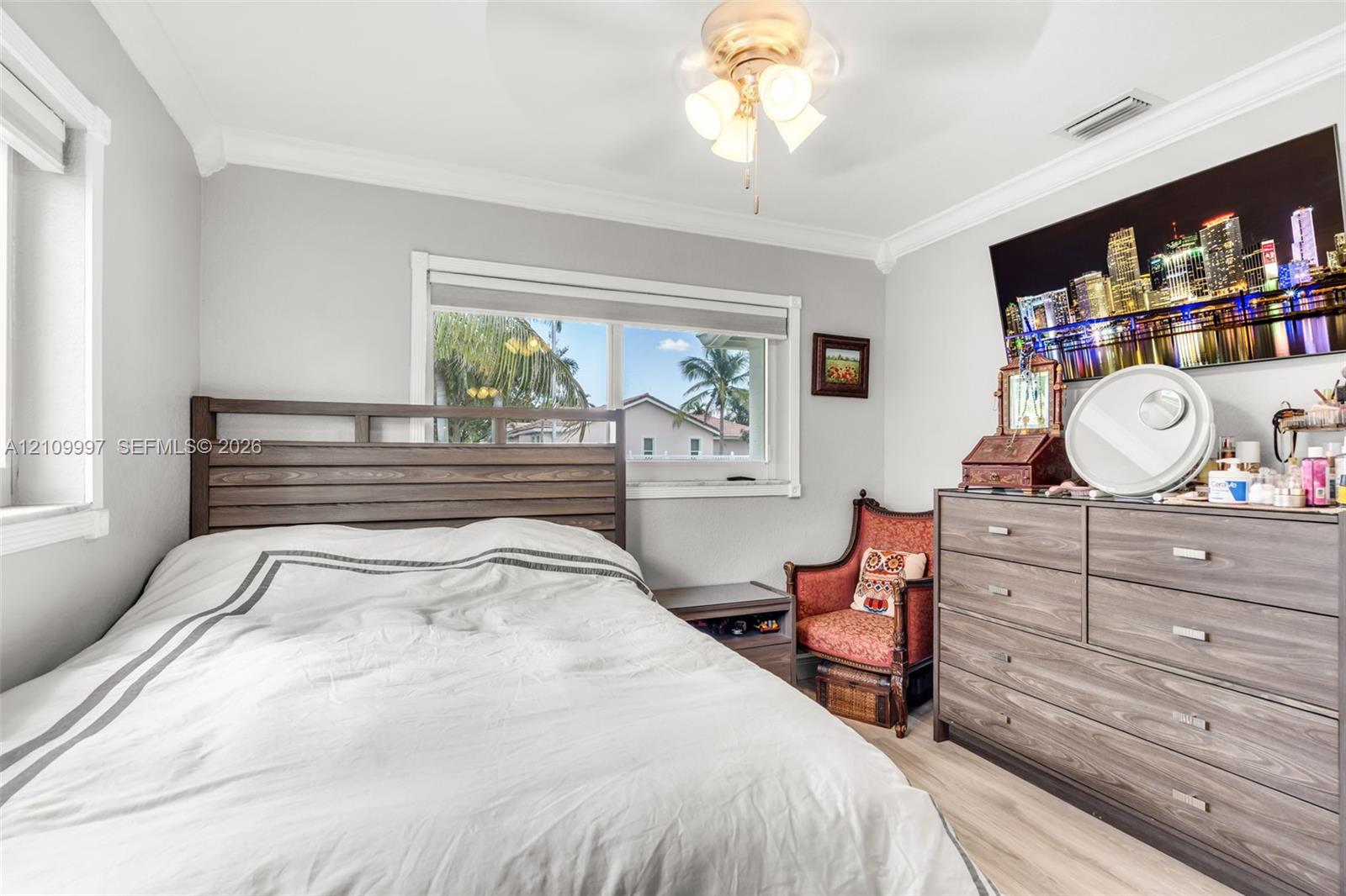 Bedroom featuring light-toned wood-finish flooring, crown molding, a central ceiling fan with integrated lighting, and dual-pane windows