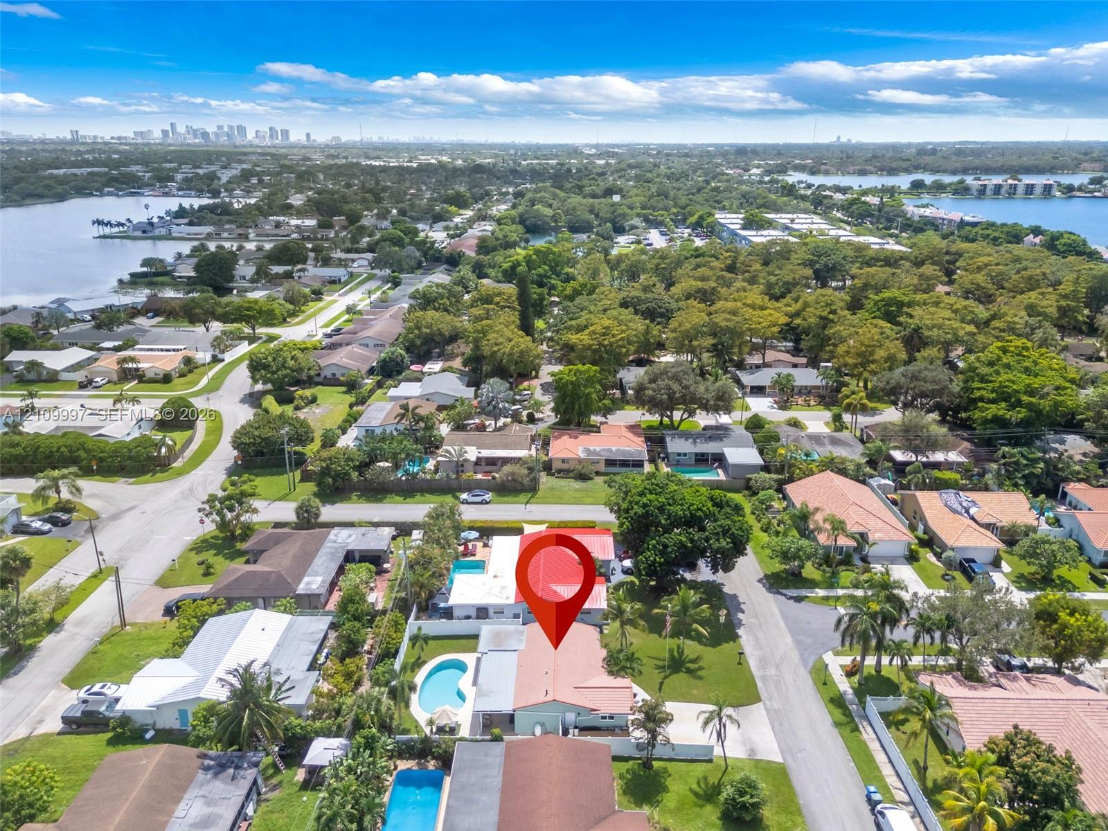Aerial perspective showcasing a residential property featuring a backyard swimming pool, expansive lawn, mature palm trees, and perimeter fencing