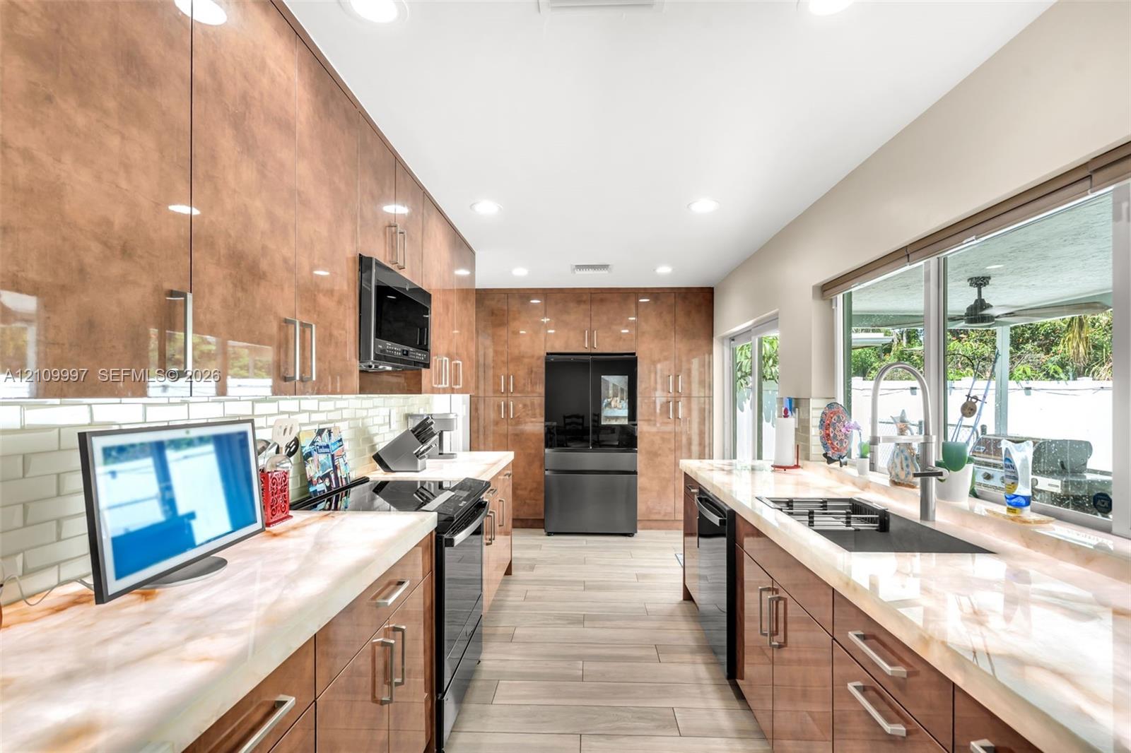 Kitchen featuring high-gloss slab cabinetry, light-toned stone countertops, subway tile backsplash, recessed lighting, and wood-finish tile flooring