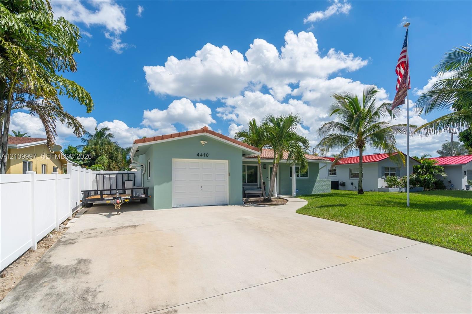 Single-story exterior featuring a light green stucco facade, a concrete driveway, a one-car garage, and a white privacy fence