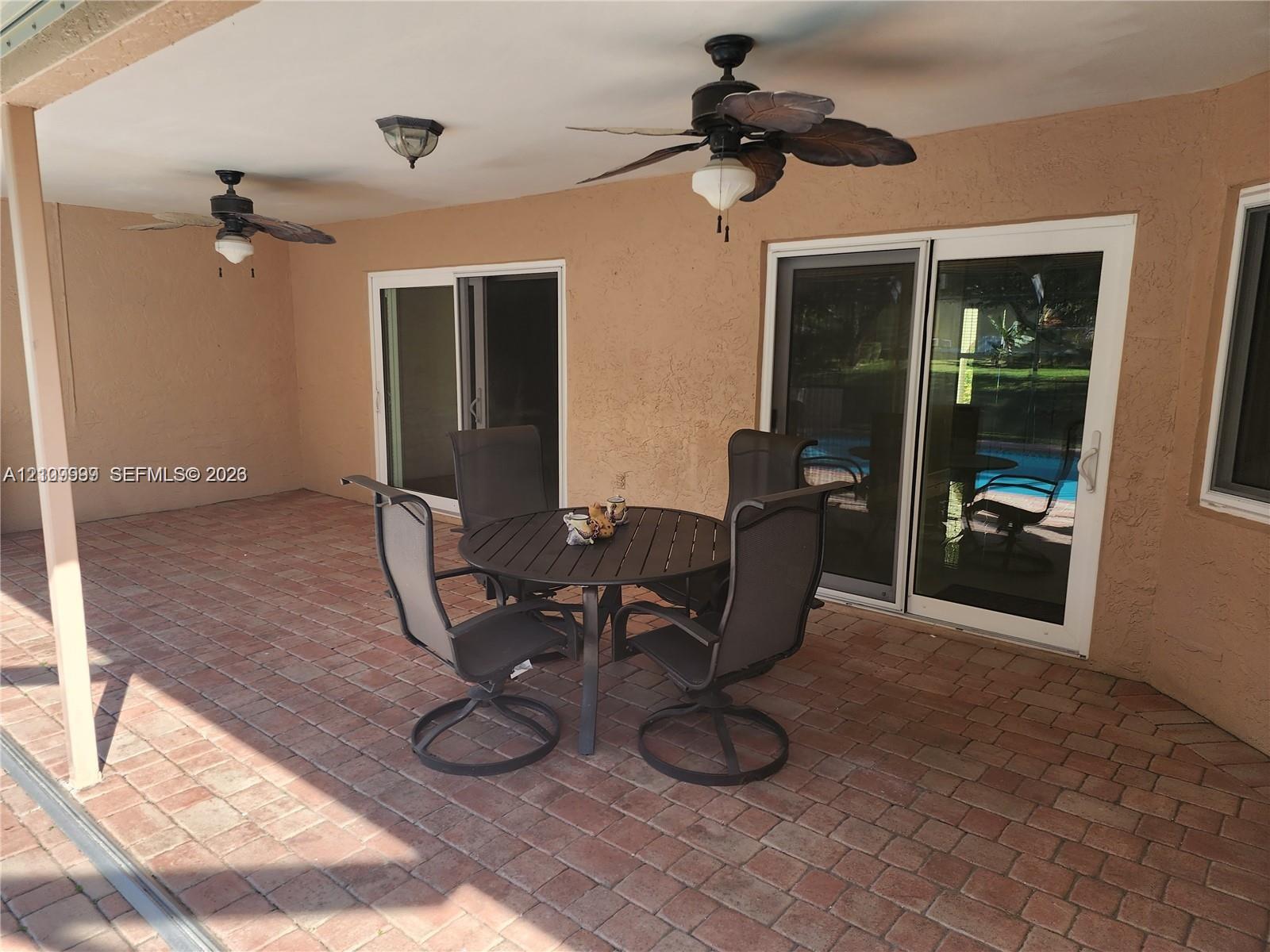Covered patio featuring brick pavers, dual ceiling fans with integrated lighting, and double sliding glass doors