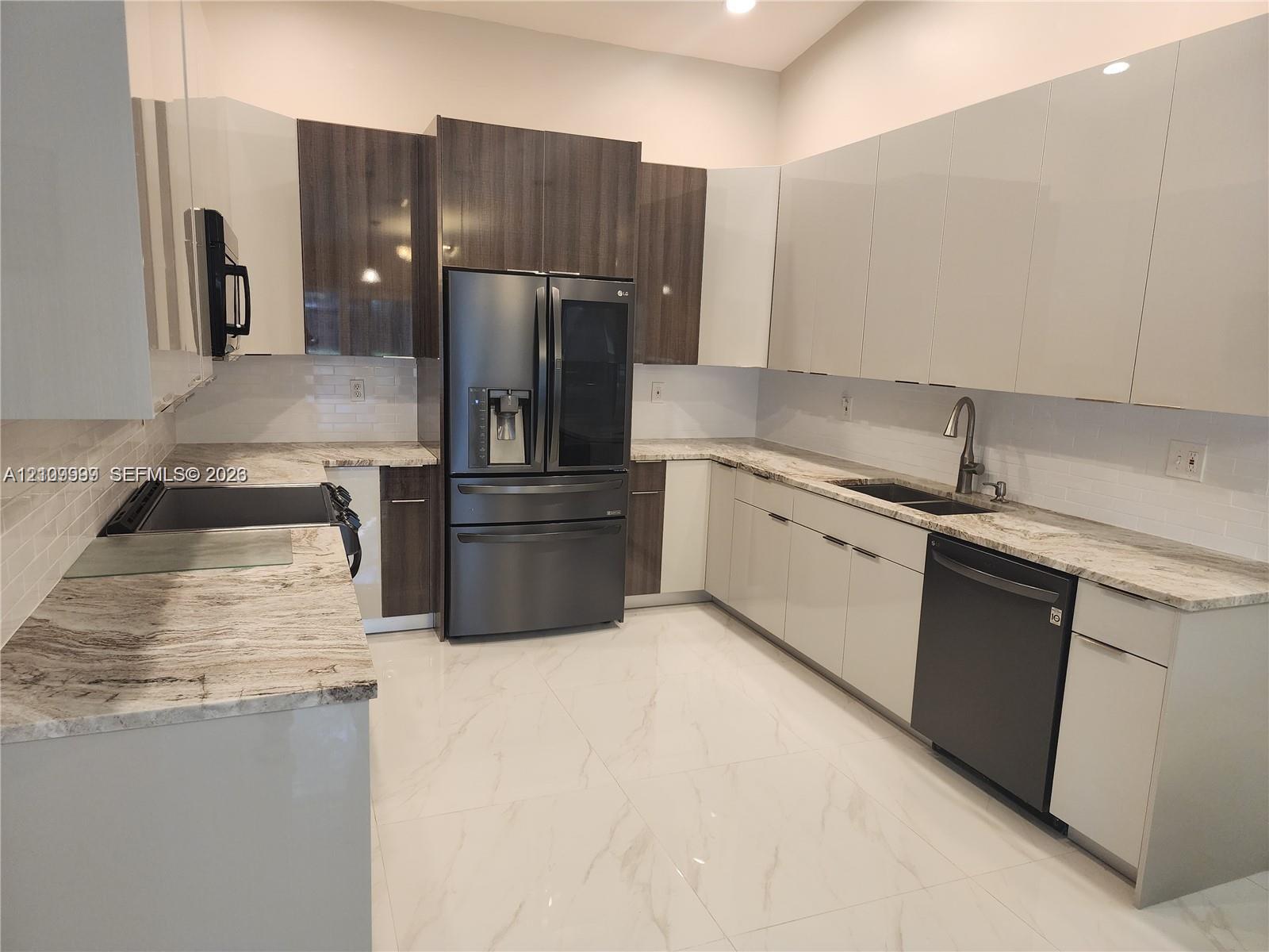 Kitchen featuring two-tone cabinetry with high-gloss finishes, stone countertops, large-format tile flooring, a double-basin undermount sink, and stainless steel appliances
