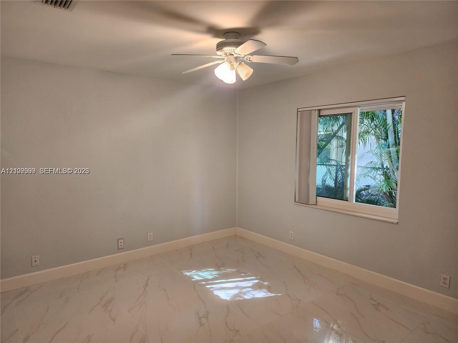 Neutral interior featuring polished stone-finish flooring, a ceiling fan with integrated light fixture, and a sliding window
